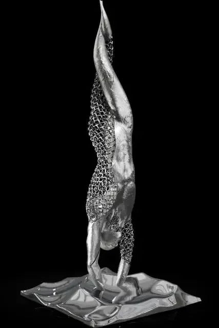 Metallic sculpture of a figure in a headstand on a white background